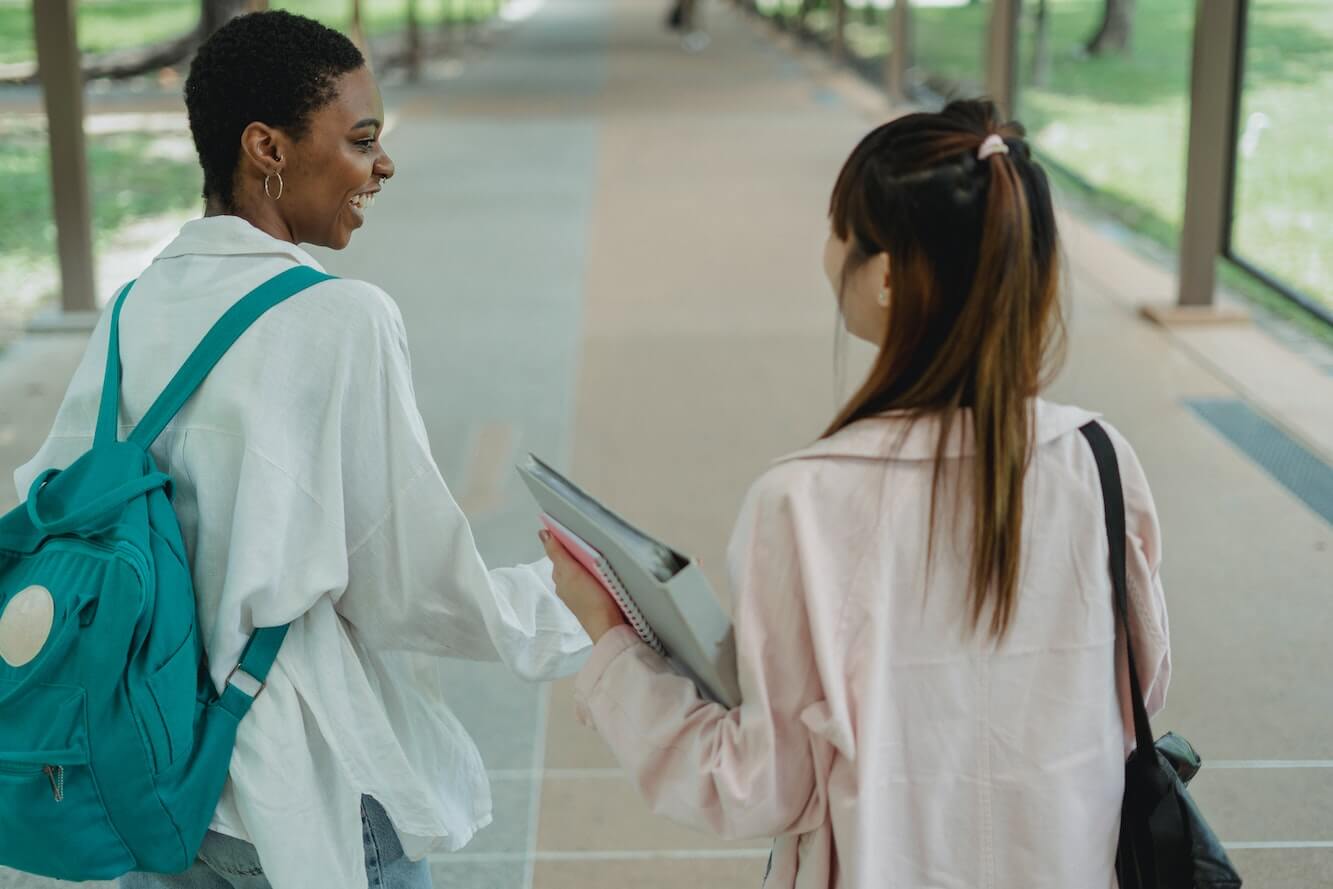 Two women college students with backpacks talking. 
