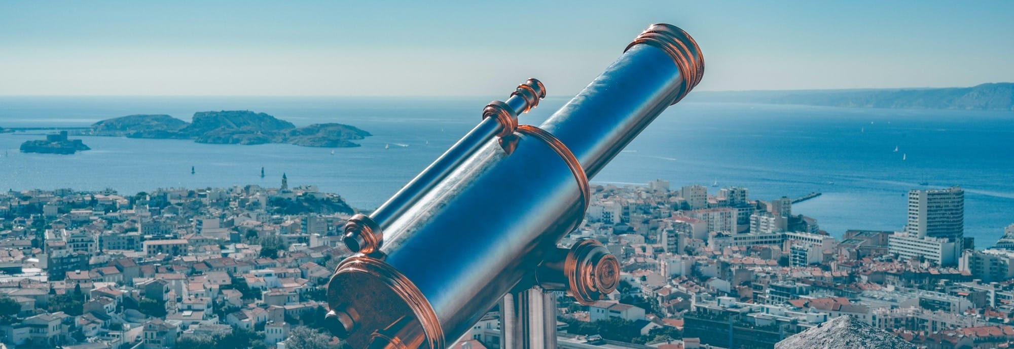 blue and brown coin-operated telescope viewing city with high-rise buildings, blue sea, and mountain under blue and white sky