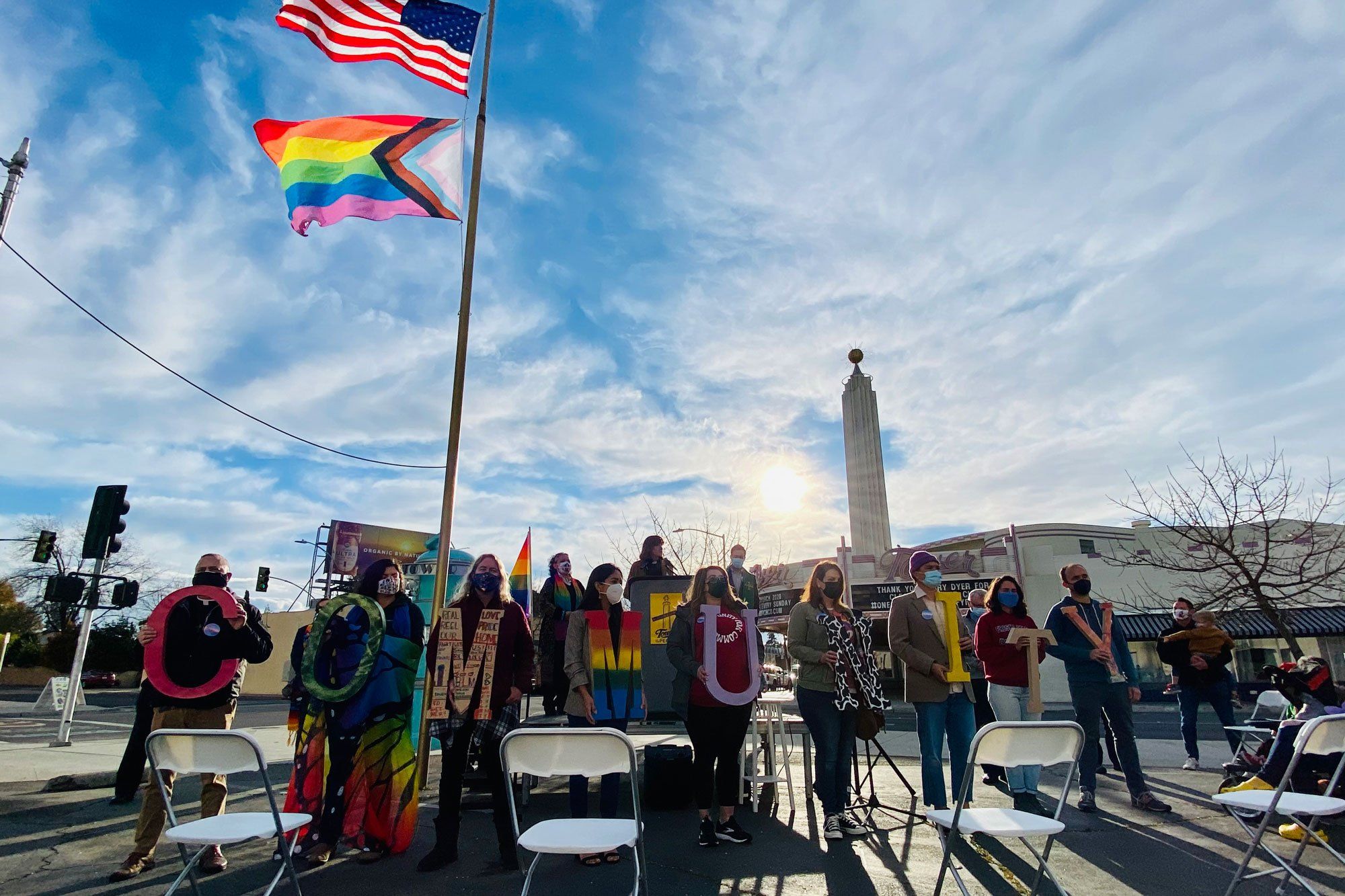 Community members line up holding individual letters to spell out the word “community” before a crowd of supporters and the media.