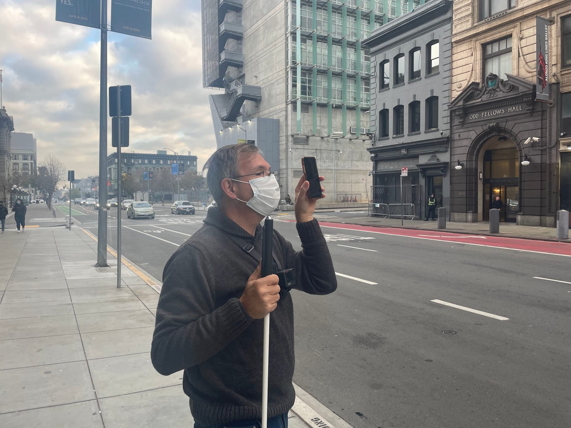 A research participant with a white cane holding up a phone on a Market Street sidewalk.