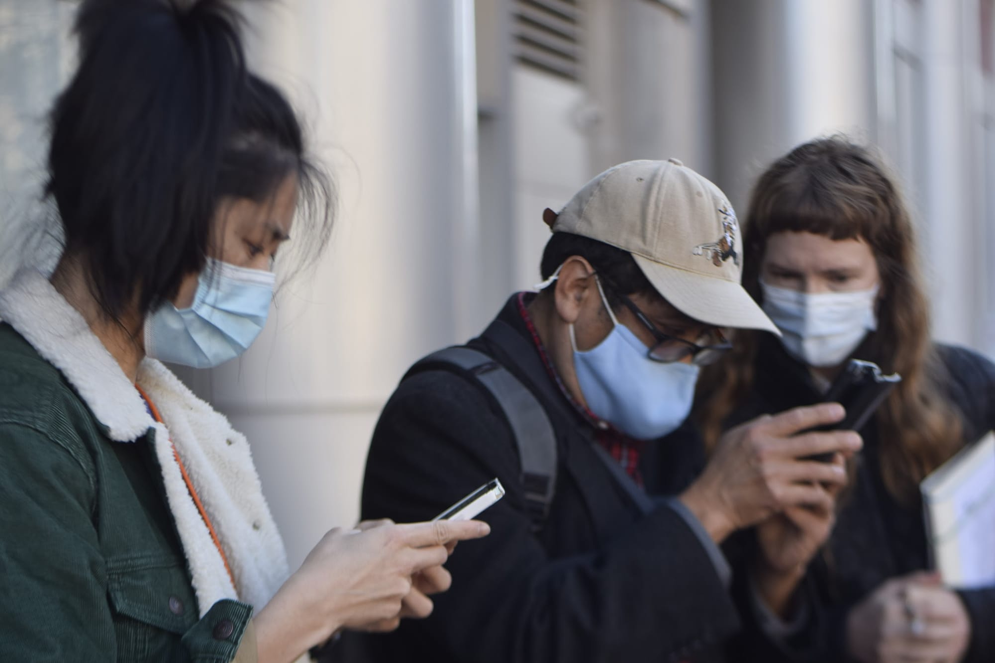 Three masked researchers checking phones together on a sidewalk during a field session.