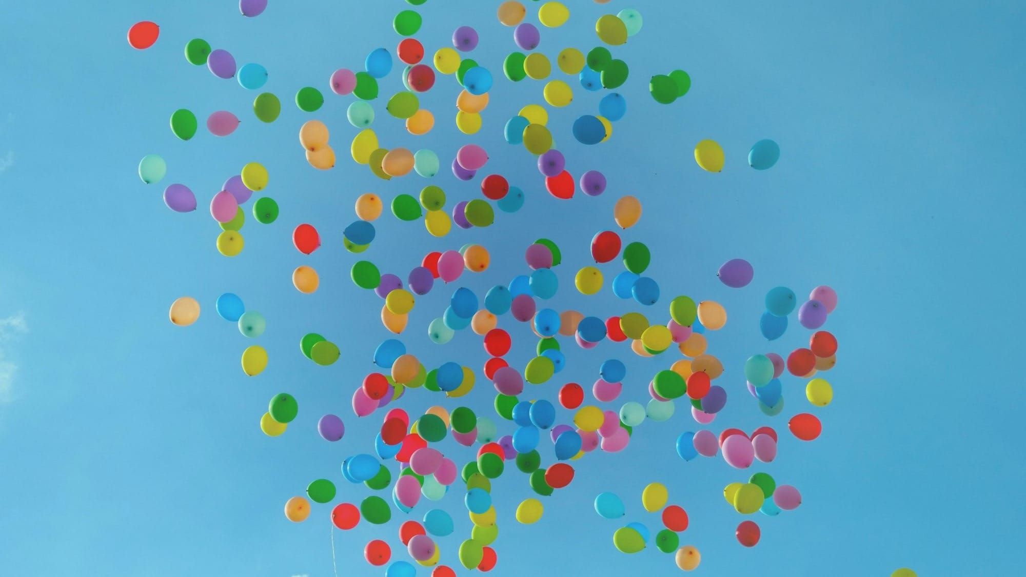 Multi-coloured balloons rising up into the air against a bright blue sunny sky