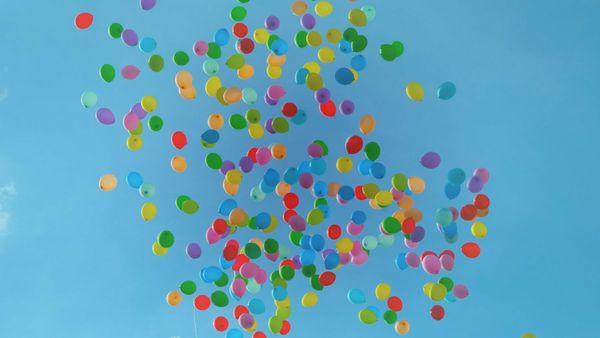 Multi-coloured balloons rising up into the air against a bright blue sunny sky