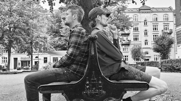 Two men sat back to back on outdoor benches in a city courtyard