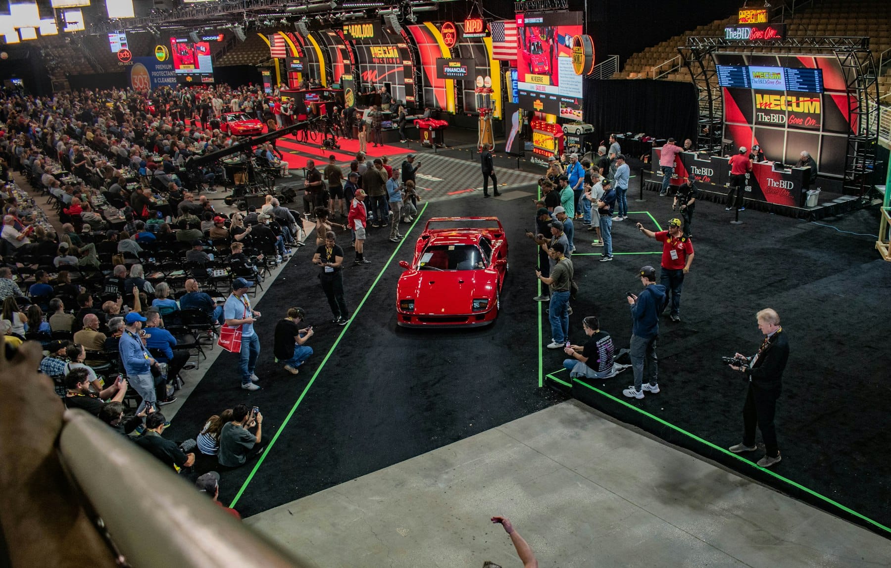 Red sports car driving through a crowd of bidders at a collector car auction