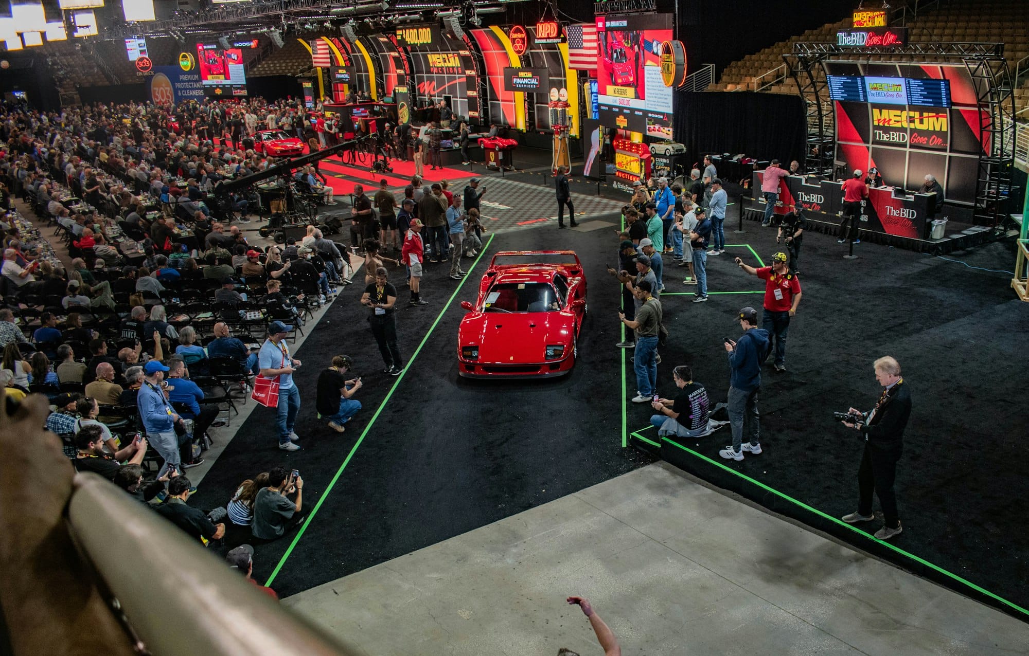 Red Ferrari F40 crossing a live collector car auction floor surrounded by bidders