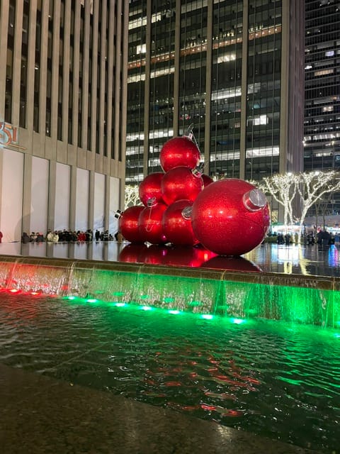 Giant red Christmas ornament sculptures stacked in a fountain plaza at Rockefeller Center in New York City at night.