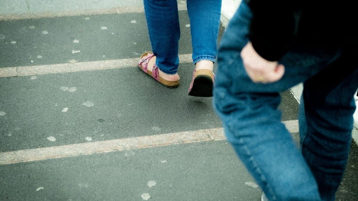 A close-up photograph of a person wearing cuffed blue jeans and sandals walking down outdoor concrete steps.