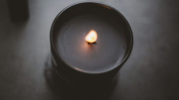 A close-up, soft-focus photograph of a single candle lit on a dark table, with a warm golden flame casting a gentle glow against a dim background.