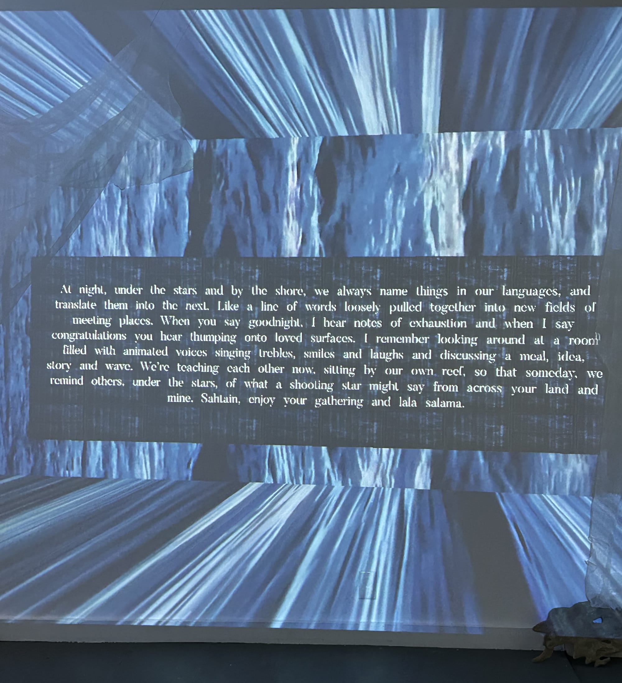 Digital projection featuring a long passage that starts with: "At night, under the stars and by the shore, we always name things in our languages, and translate them into the next."