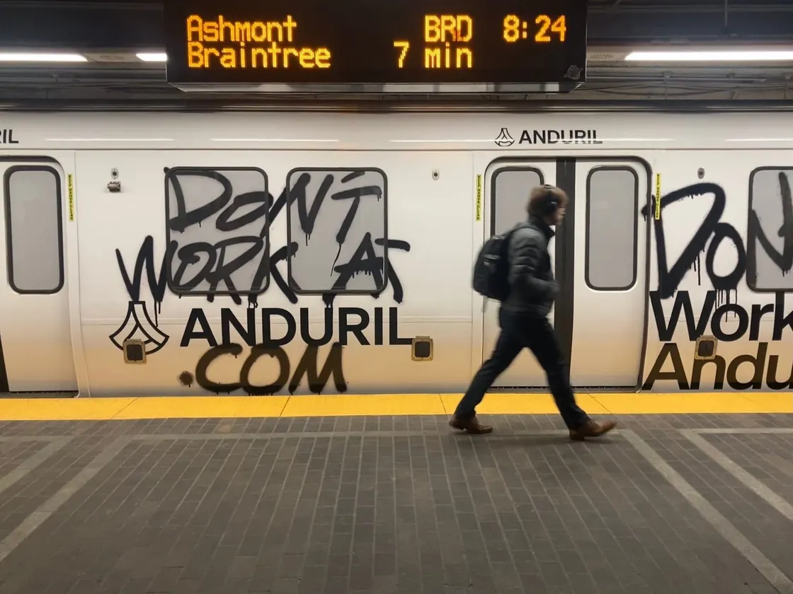 Boston subway wrapped in Anduril’s bold “Don’t Work Here” graffiti-style recruitment ad. Commuter walks past campaign.