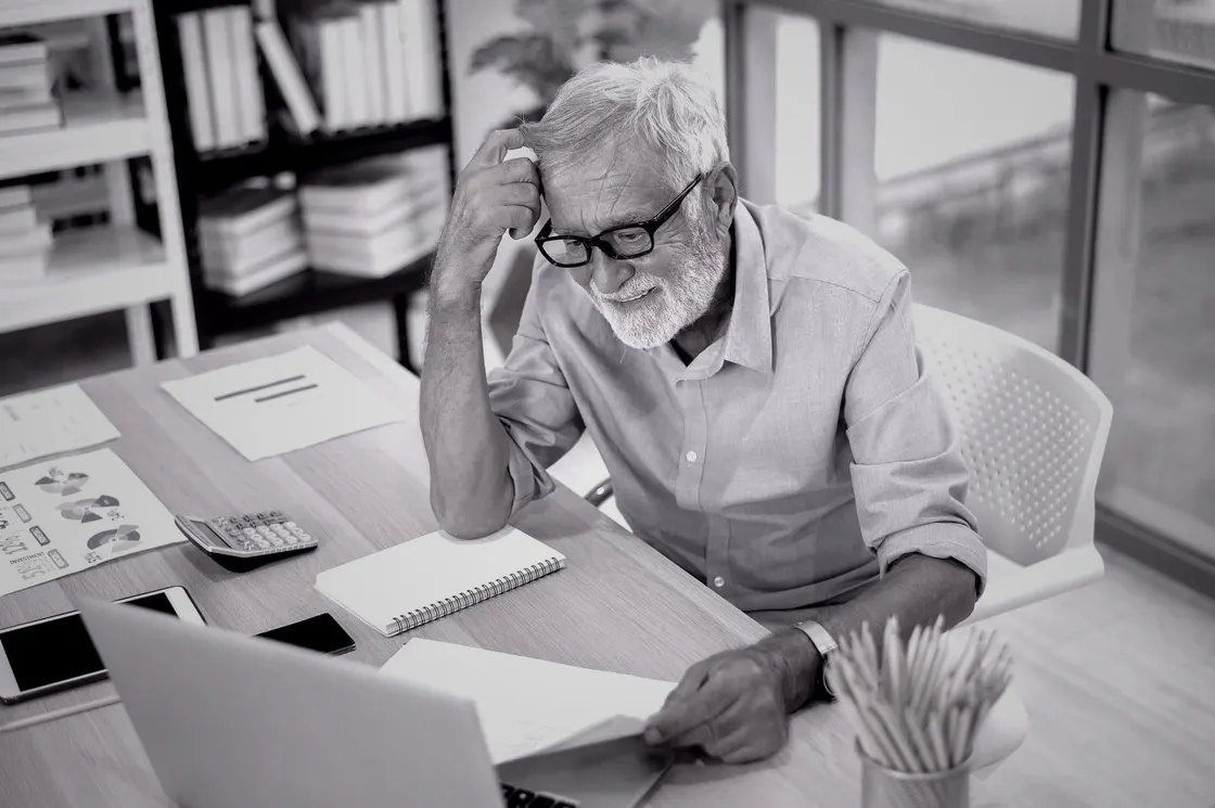 Older man in business attire looking frustrated at a laptop in an office setting, representing age discrimination in algorithmic hiring processes.
