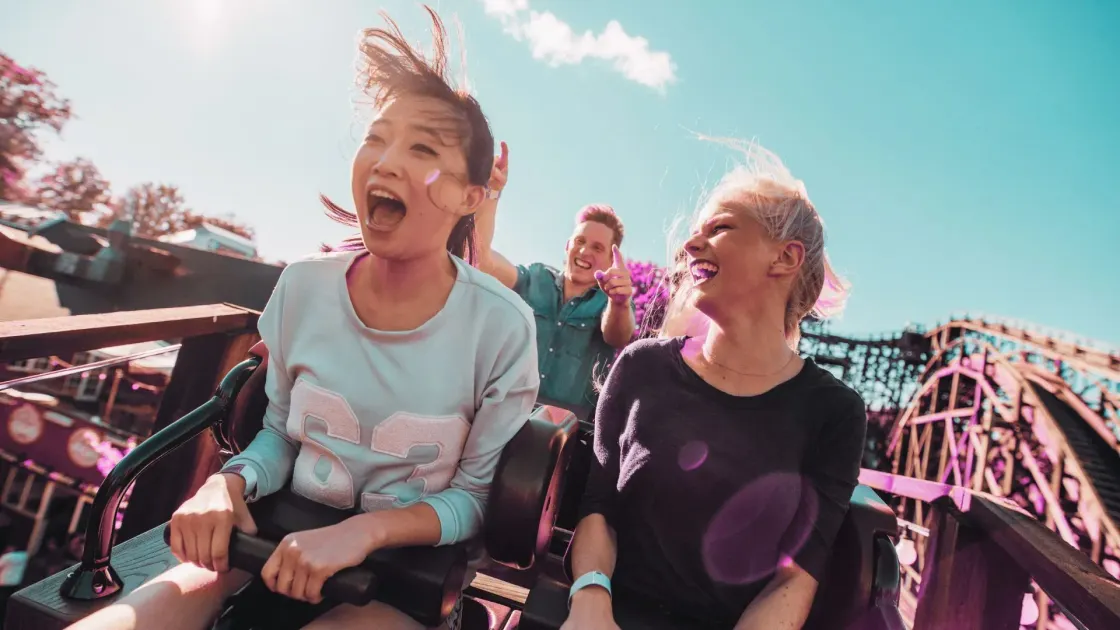 Three friends hurtle down a wooden roller coaster on a sunny day, laughing and shouting, symbolising the wild ups-and-downs of this week’s AI-driven job market.
