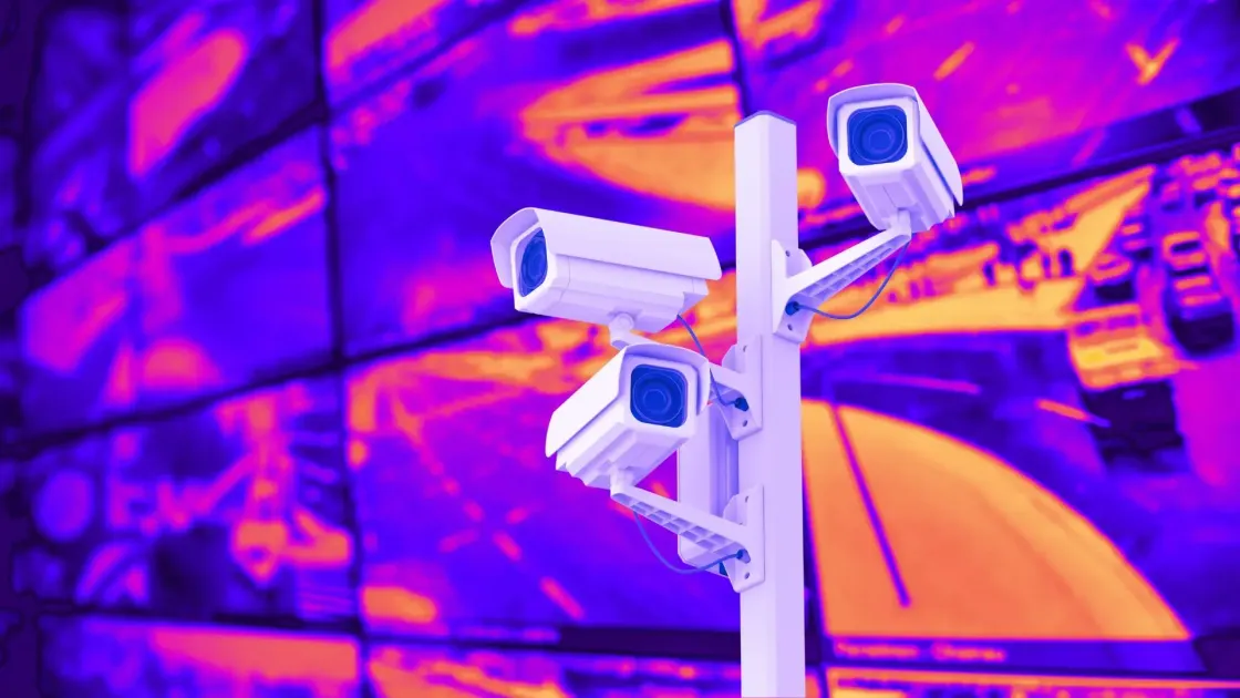 Four white CCTV cameras mounted on a pole in front of a neon purple-orange video wall, symbolising workplace attendance monitoring and office surveillance.