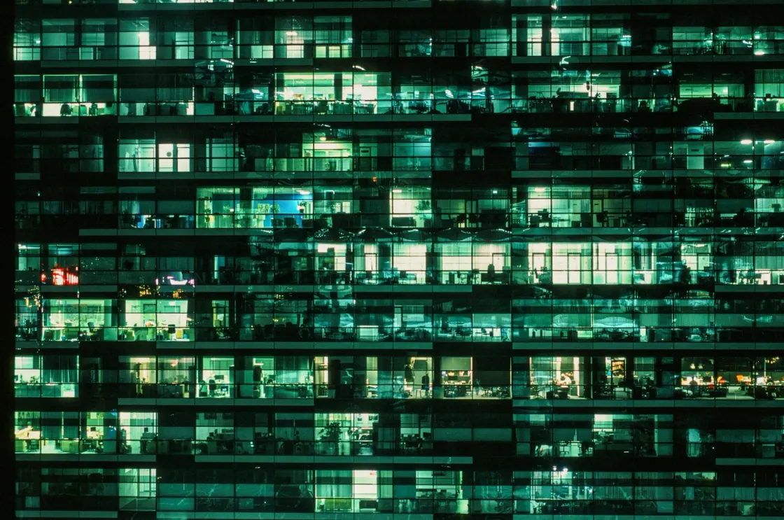 Night view of a modern office building with illuminated windows, representing white-collar jobs and the future of work under threat from artificial intelligence.