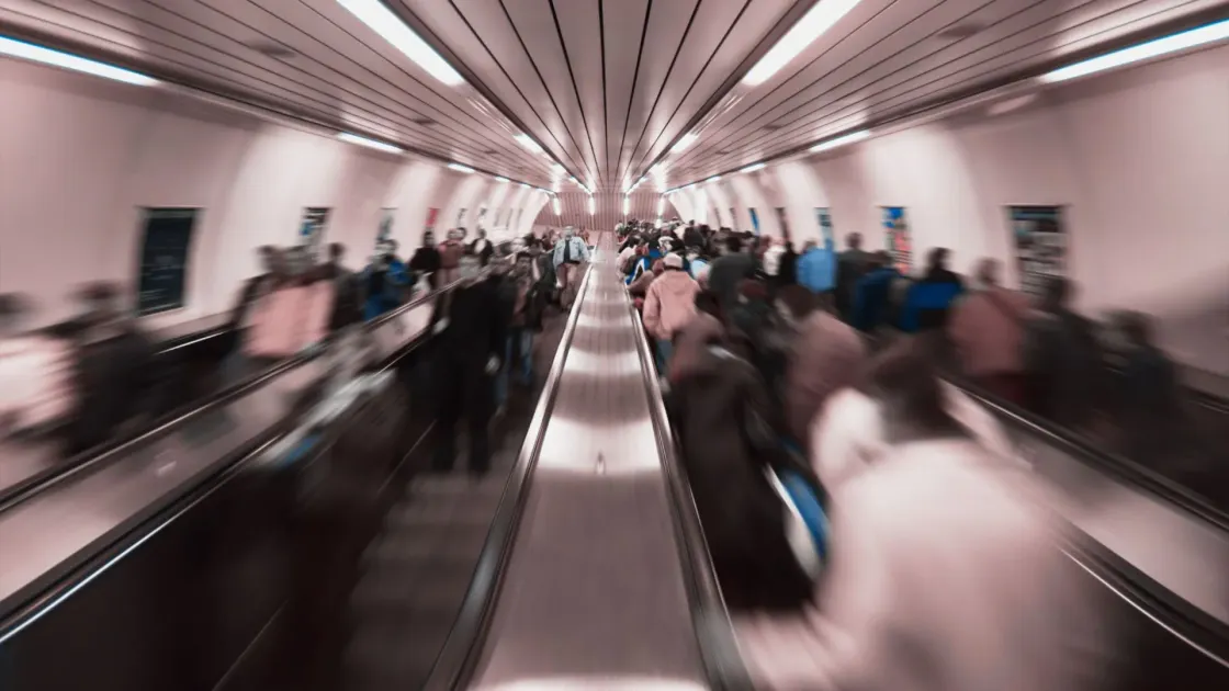 Motion-blur crowds on subway escalators at rush hour.