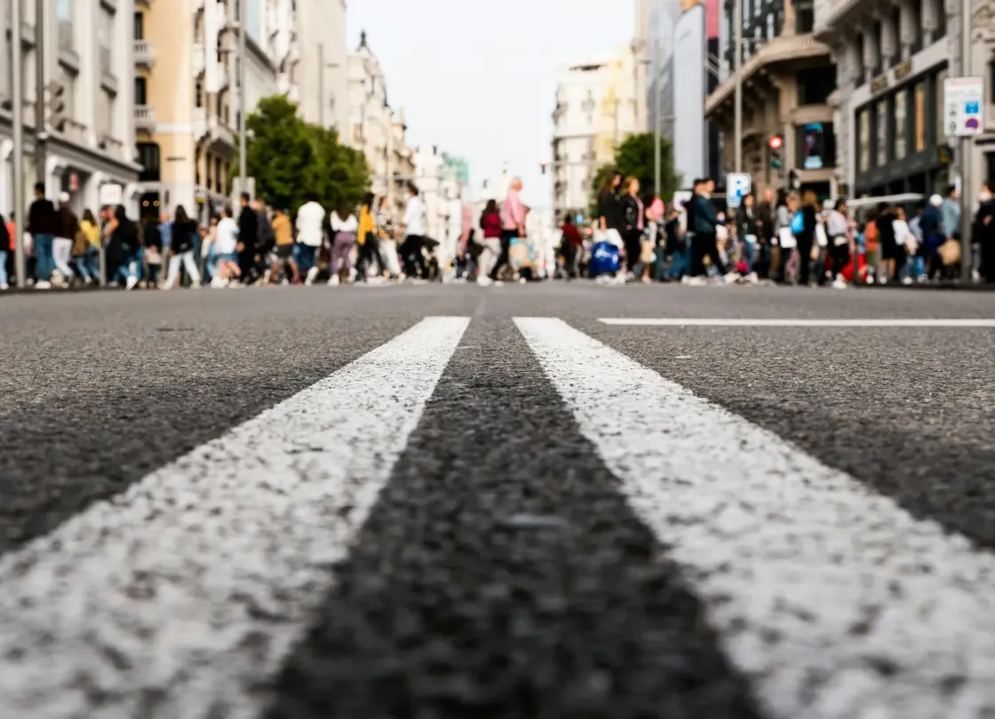Low-angle view of a European city street with pedestrians crossing in the distance, symbolising varied cultures and regulations shaping Europe’s 2025 employer branding.