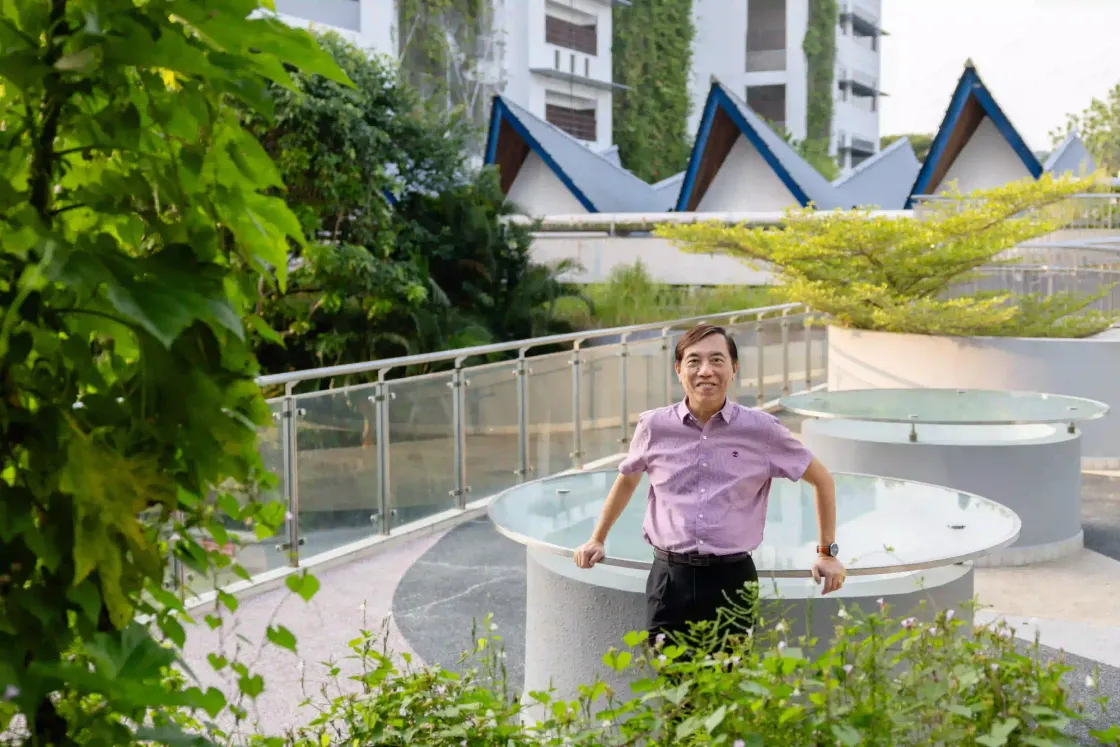 Kevin Chua standing outdoors on a modern school campus, smiling with greenery and architecture in the background.