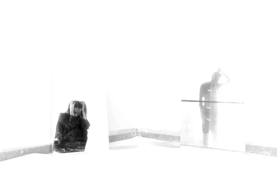 A person reflected in mirrors holding their head, symbolizing self-reflection and emotional depth, representing clarity and empathy in the modern workplace.