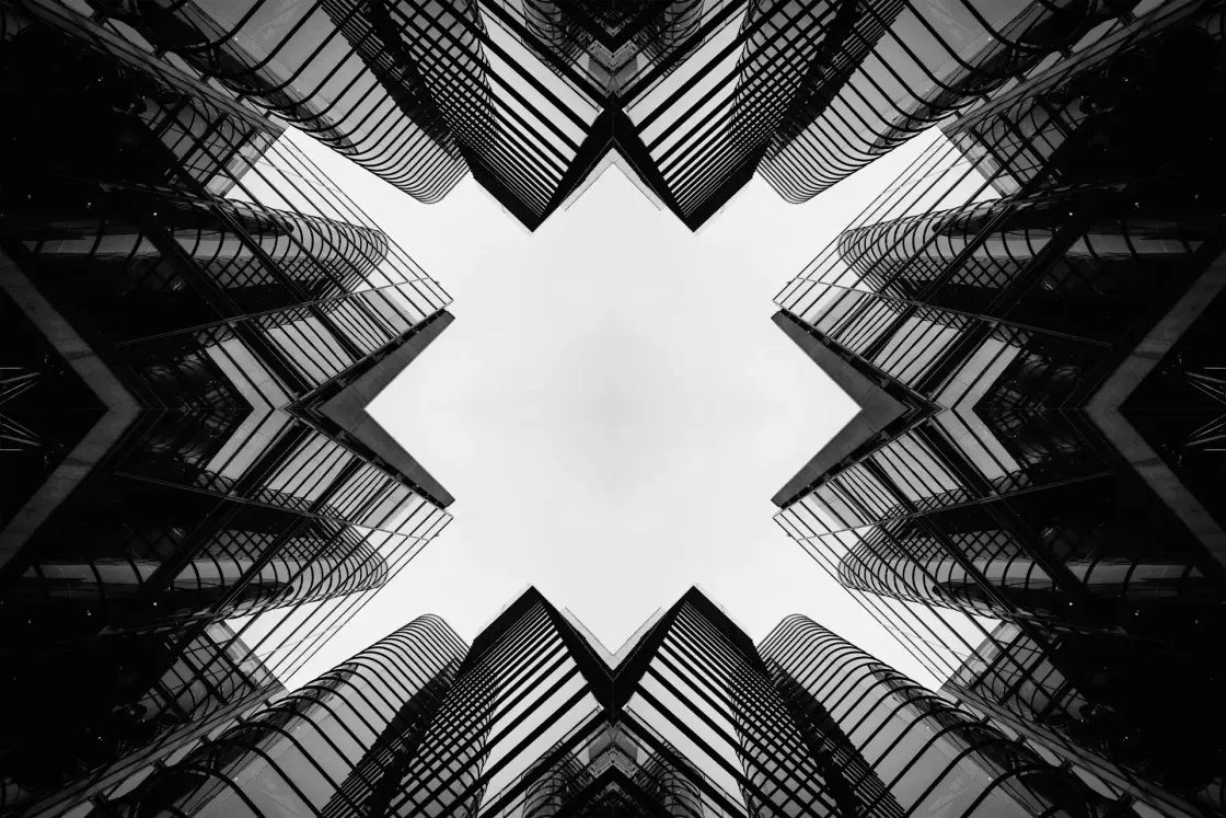 Symmetrical black and white cityscape looking up at mirrored glass office towers forming an X-shaped frame.