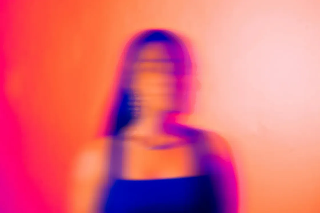 Blurred silhouette of a person in profile against vivid pink, orange and blue light, suggesting uncertainty, identity shift and the human impact of AI at work.
