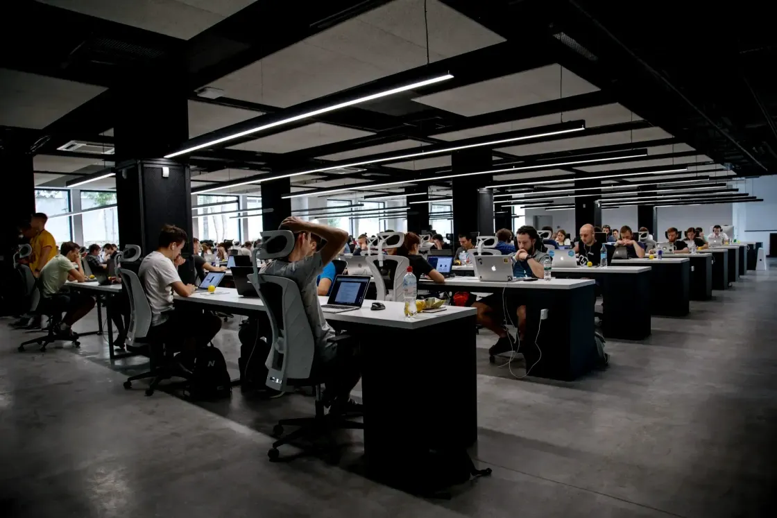 Employees working at long shared desks in a modern open-plan office, illustrating the cautious, risk-averse mood shaping the Big Stay.