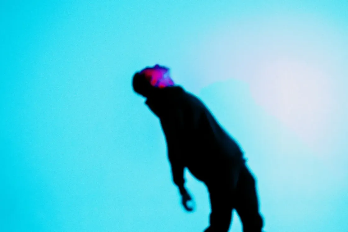 Blurred silhouette of a figure leaning under weight, lit in cyan and red, representing unaddressed employee strain.