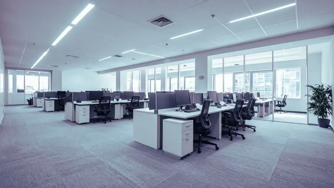 An empty open-plan office with rows of desks and chairs under bright ceiling lights, suggesting unused workspace after job cuts or reduced headcount.