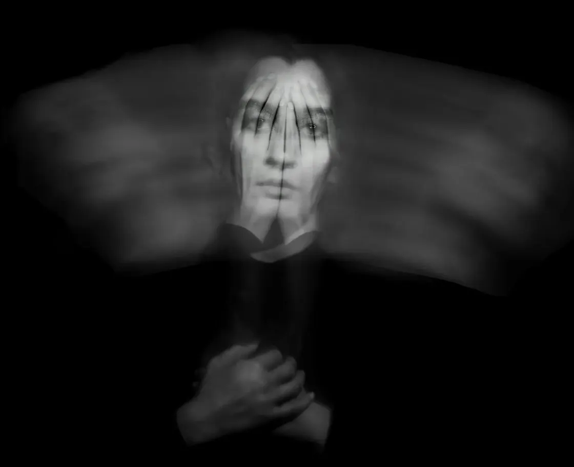 Black-and-white blurred portrait of a person covering their face with both hands, representing the stress, instability, and invisibility experienced by underemployed workers.
