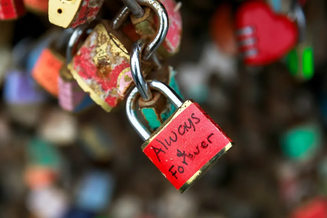Close-up of several weathered padlocks hanging together, including a red lock marked “always forever”