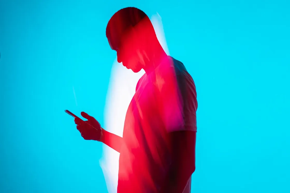 Silhouette of a person looking at a smartphone, lit in red against a bright blue background.