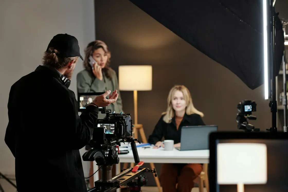A production team records two employees in a studio using cameras, lighting and monitoring equipment.