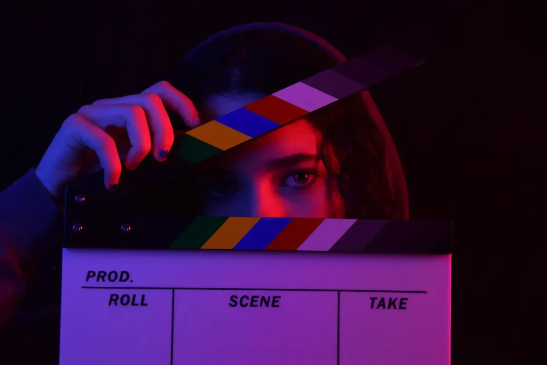 Person peering over a film clapperboard in red and blue light, illustrating scripted authenticity in employer branding
