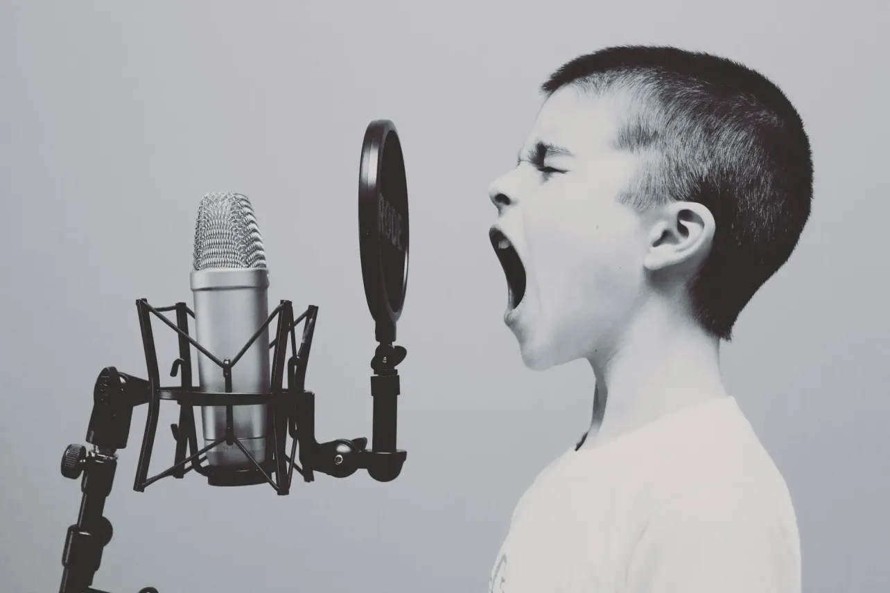 Black and white photo of a young boy yelling into a professional microphone, evoking the image of a CEO making loud but ill-judged public statements.