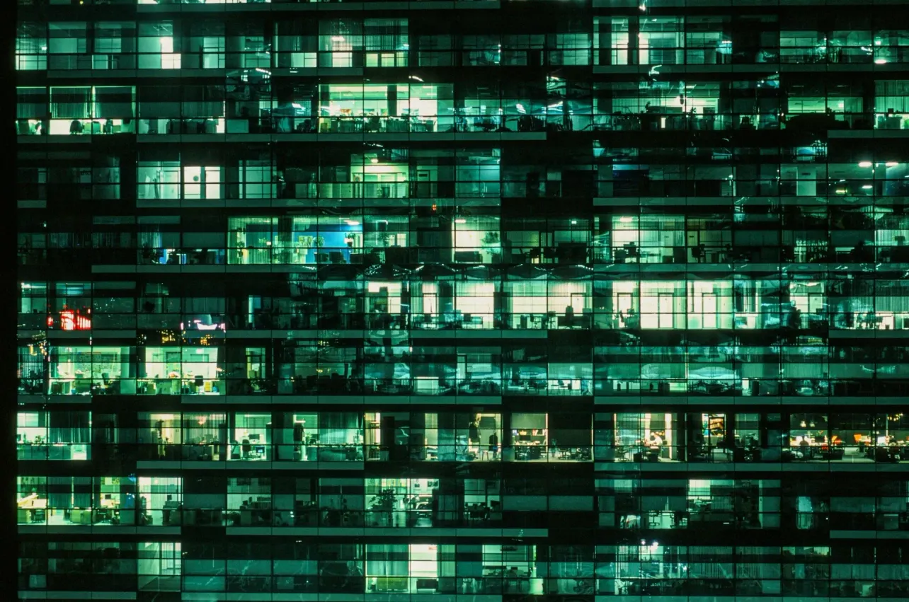 Night view of a modern office building with illuminated windows, representing white-collar jobs and the future of work under threat from artificial intelligence.