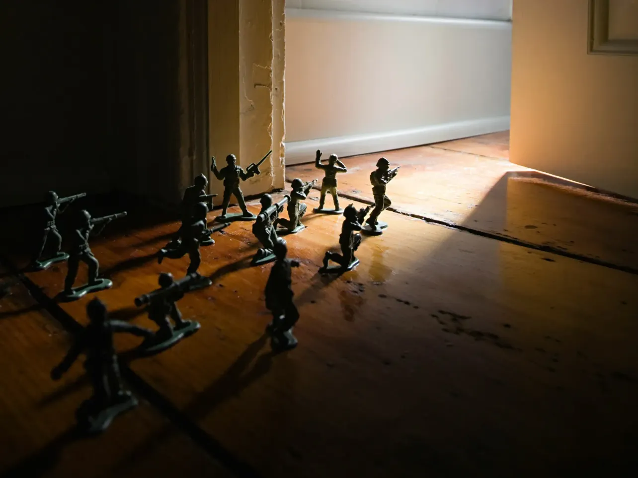 Plastic toy soldiers advancing across a wooden floor toward an open doorway with bright light streaming in.