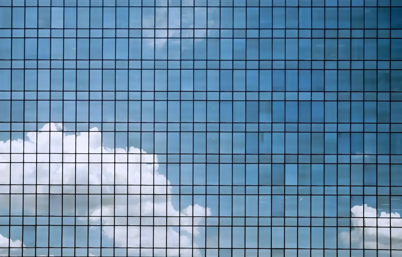 Clouds and blue sky reflected in the grid of a modern glass office building facade.