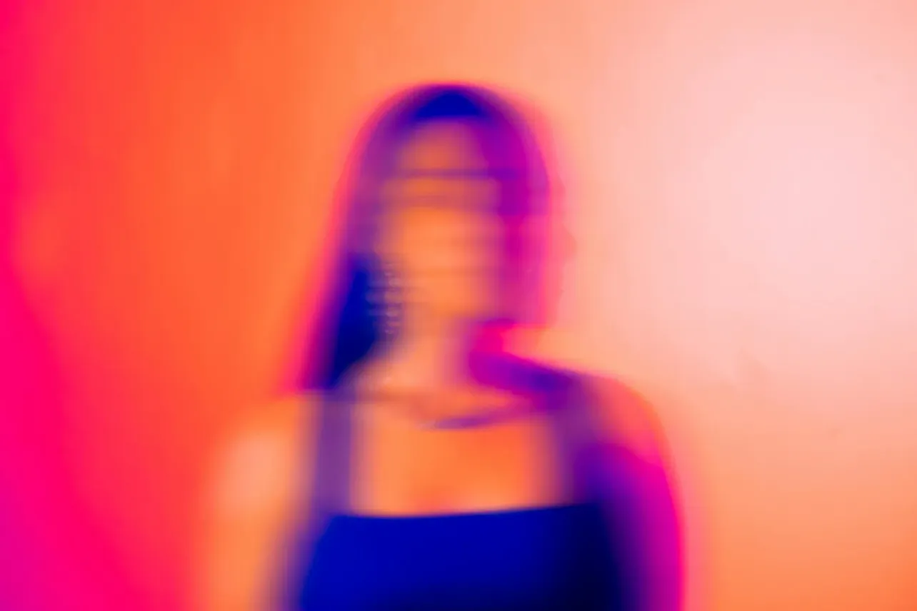 Blurred silhouette of a person in profile against vivid pink, orange and blue light, suggesting uncertainty, identity shift and the human impact of AI at work.