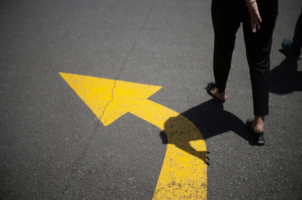 A person walks past a large yellow directional arrow painted on asphalt, symbolising strategic direction, momentum and decision-making in employer branding.