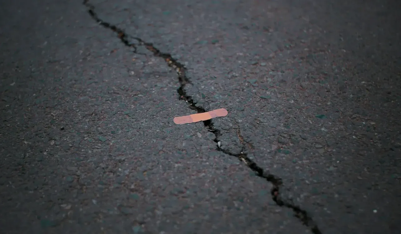 A bandage placed over a crack in dark asphalt, symbolising a broken hiring system held together by temporary fixes.