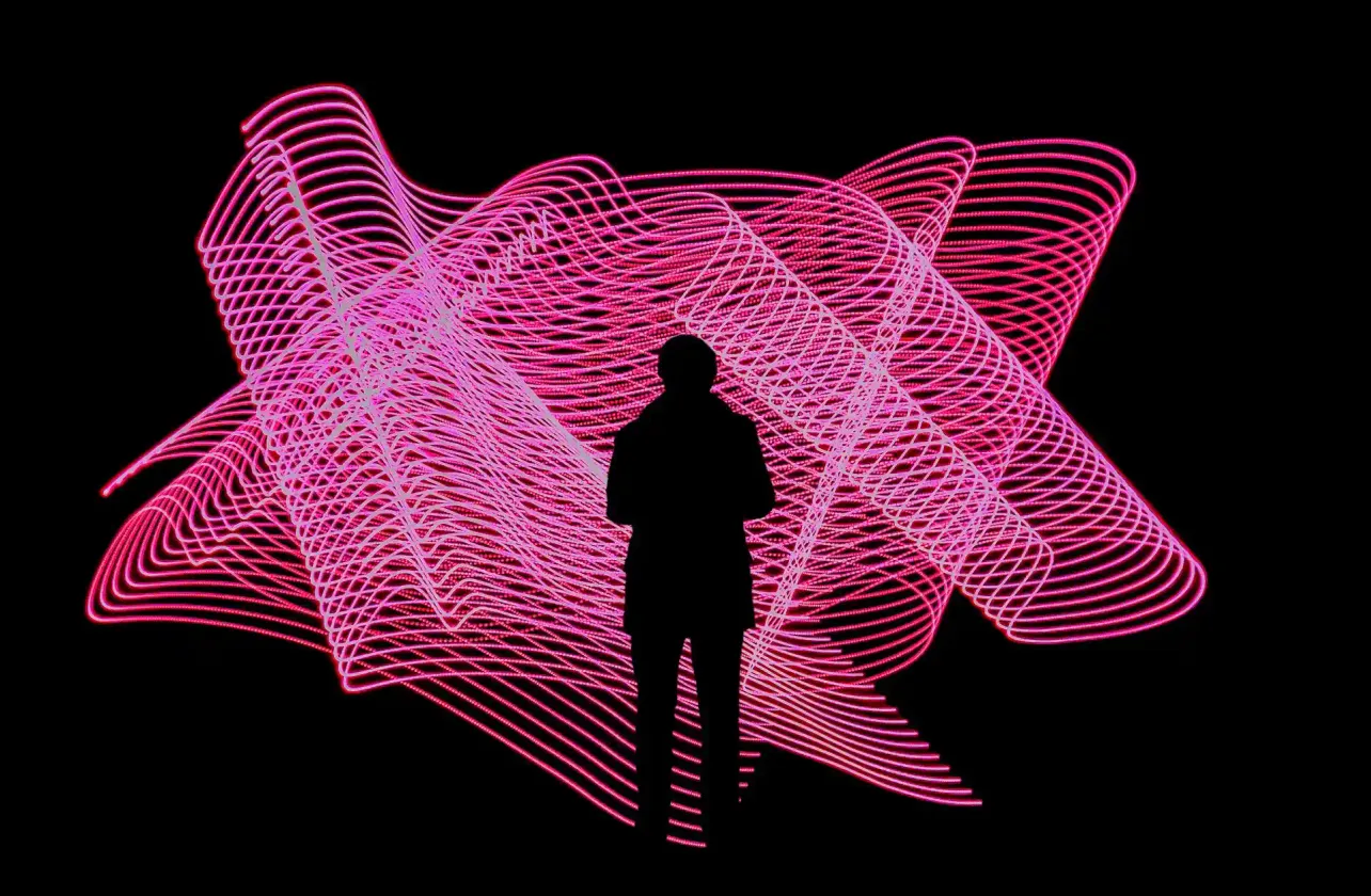 A lone human silhouette stands inside vast pink and white algorithmic light trails on black, evoking an individual within the swirling currents of an AI-shaped labour market.