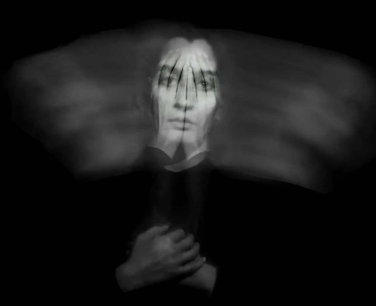 Black-and-white blurred portrait of a person covering their face with both hands, representing the stress, instability, and invisibility experienced by underemployed workers.
