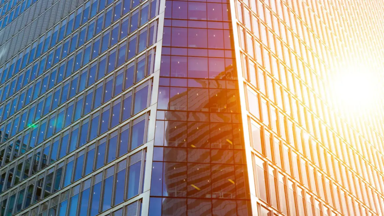 Glass office building exterior on a hot summer day, sun reflected off the facade, no people visible.