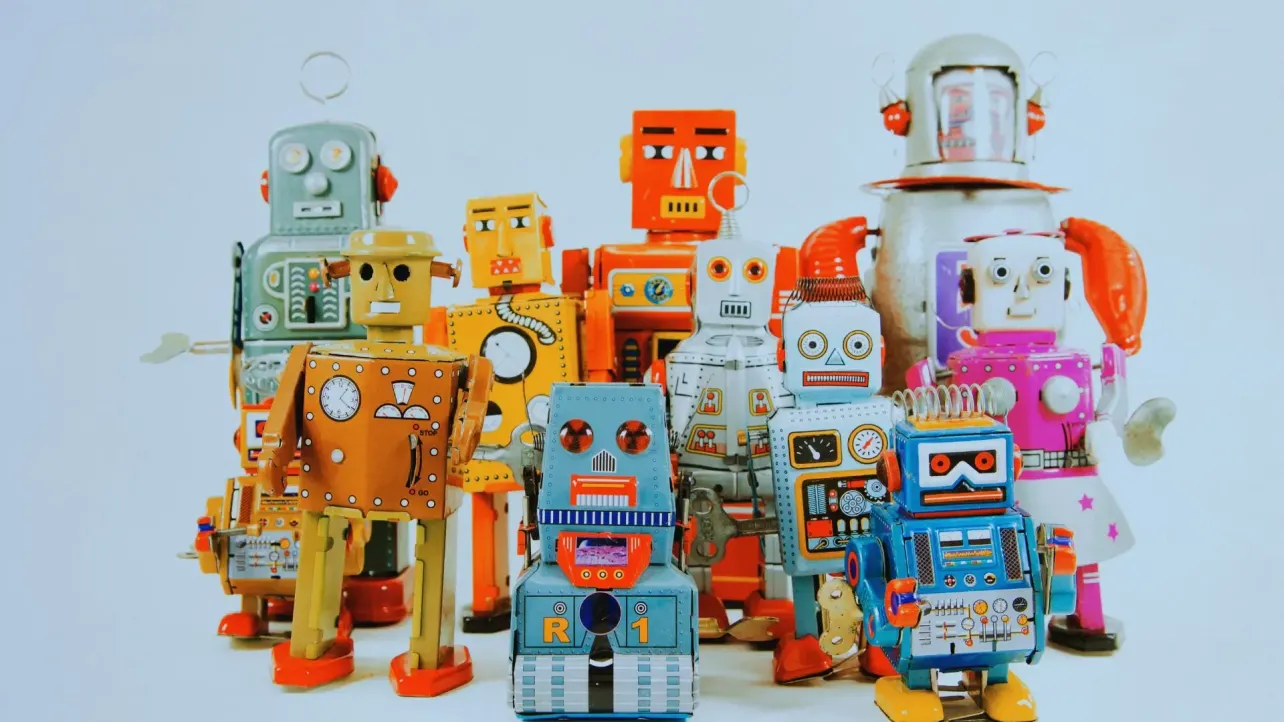 A group of colourful toy robots standing together against a plain background, representing workplace AI tools that need human supervision and management.