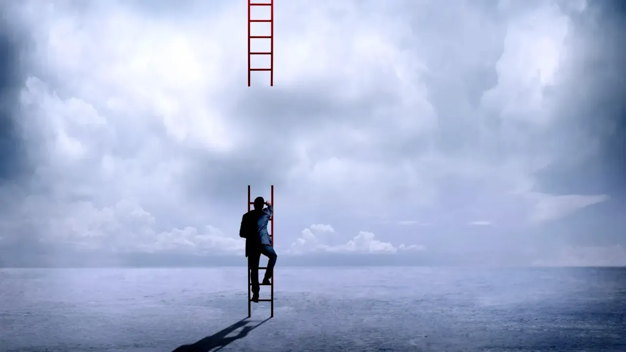 A person in a suit climbing a red ladder toward a second ladder that stops short in the clouds, symbolising a broken career ladder and a narrowing path upward.