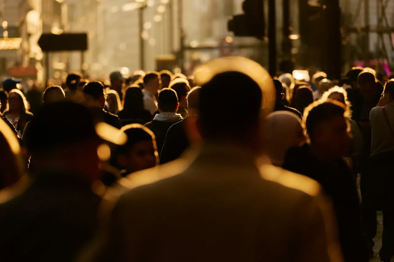 A crowded city street at golden hour, with people moving through a dense, backlit flow, illustrating scale, complexity, and the human systems behind enterprise hiring.