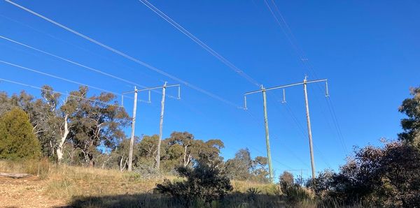 A pair of powerlines on a hill against a blue sky