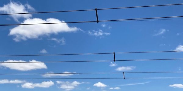 Three pairs of powerlines running horizontally across a white cloud flecked blue sky
