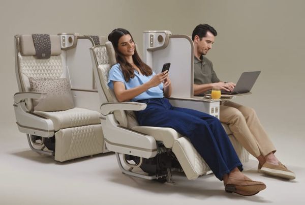 Two people sitting in new Emirates premium economy seats with the privacy shade pulled up.