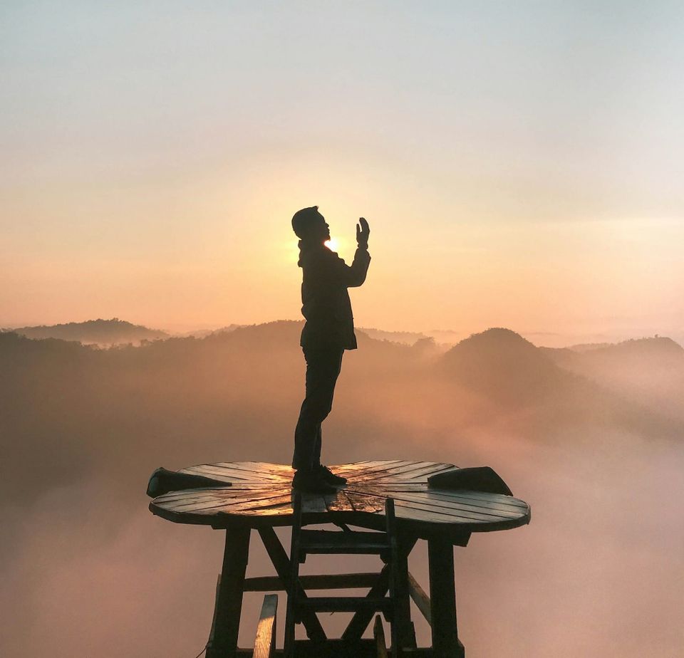 A man standing on a wooden platform praying to God.